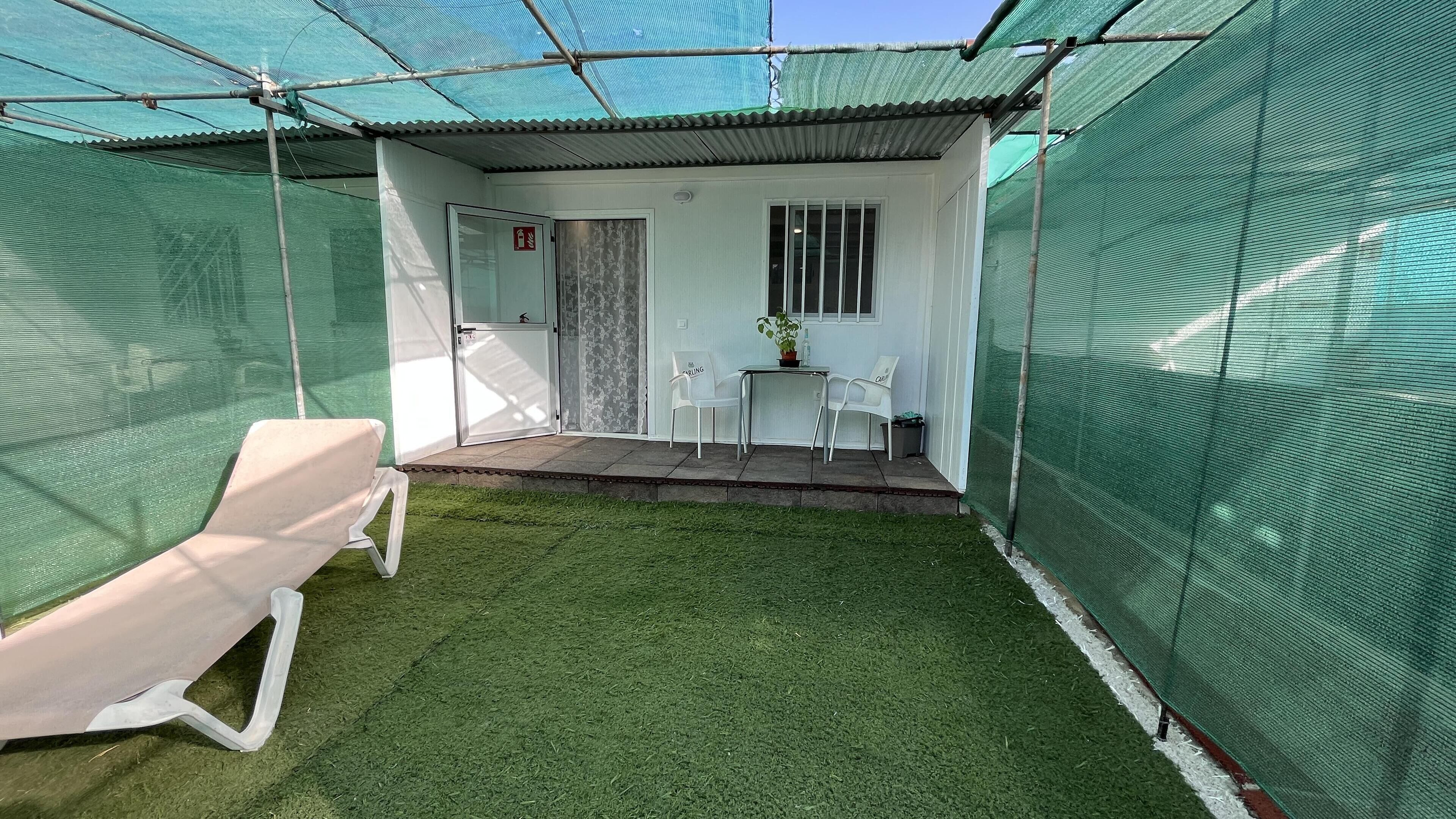 A covered outdoor area with artificial grass, a white door, and a small table with chairs.