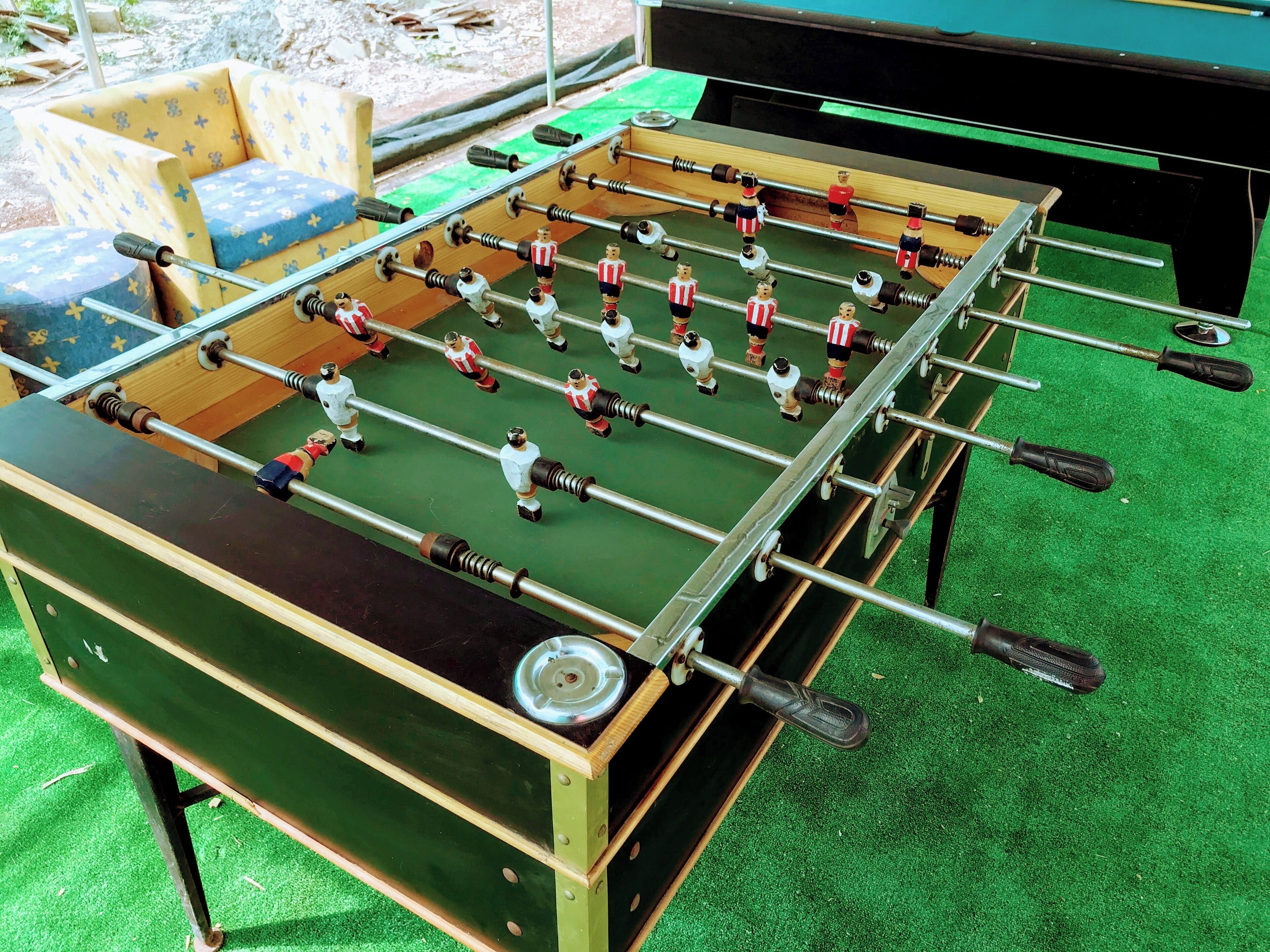 A foosball table with a green playing surface and metal rods, surrounded by a green carpeted floor.