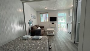 A compact living space with a sofa, a small table, a fan, and a bed with neatly folded blankets. - Modern Tiny Country House Near Fataga & Maspalomas (San Bartolomé de Tirajana)