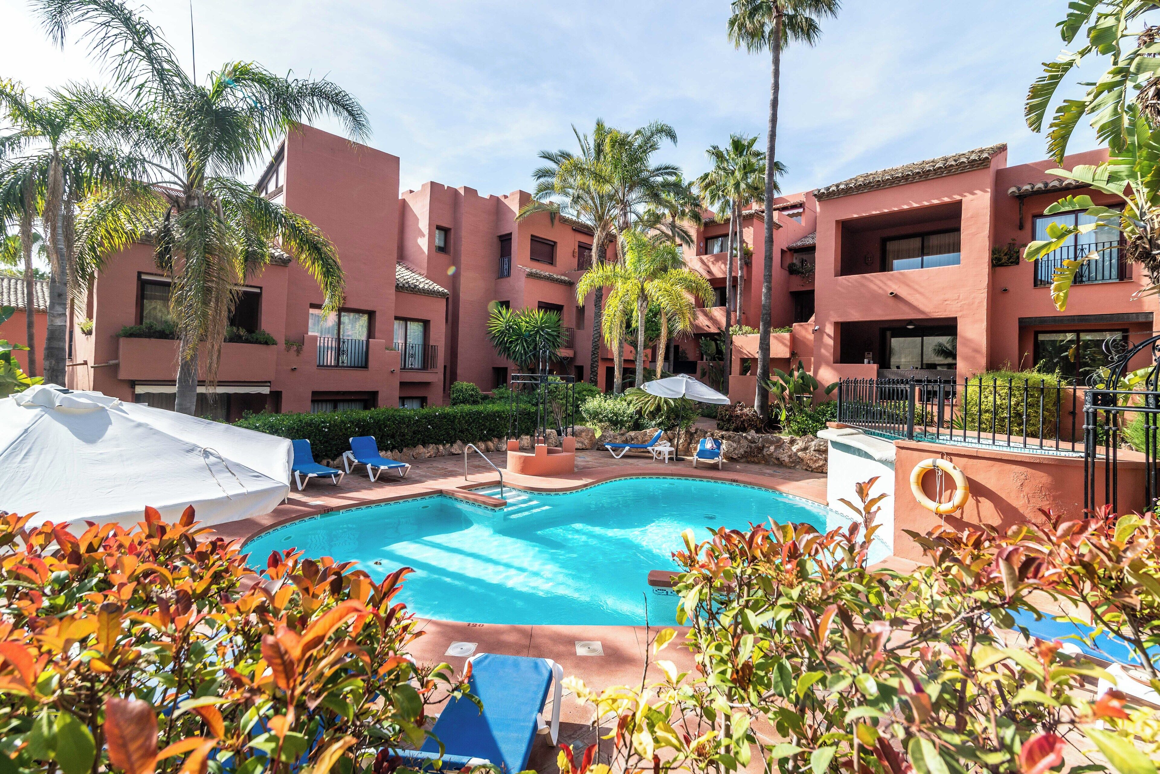 A swimming pool surrounded by palm trees and lounge chairs.