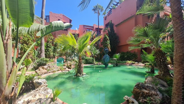 A courtyard with a small pond, palm trees, and a statue. - Luxury 2-bed Apartment Elviria - Pool, Sauna & gym (Marbella)