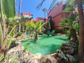 A courtyard with a small pond, palm trees, and a statue. - Luxury 2-bed Apartment Elviria - Pool, Sauna & gym (Marbella)