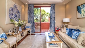 A living room with a sofa, coffee table, and a view through a glass door to an outdoor area. - Luxury 2-bed Apartment Elviria - Pool, Sauna & gym (Marbella)