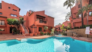 A swimming pool surrounded by buildings with balconies and palm trees. - Luxury 2-bed Apartment Elviria - Pool, Sauna & gym (Marbella)