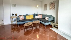 A living room with a sectional sofa, two small round tables, a floor lamp, and a woven basket. - Luxury Front Line Apartment in Isla Canela Beach (Ayamonte)