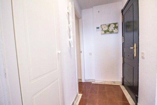 A hallway with white walls, a tiled floor, a black door with a gold handle, and a small wall-mounted light switch. - Luxury Front Line Apartment in Isla Canela Beach (Ayamonte)