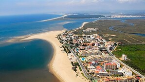 An aerial view of a coastal town with a beach, buildings, and a marina. - Luxury Front Line Apartment in Isla Canela Beach (Ayamonte)