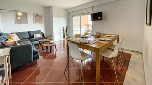 A modern living room with a sofa, coffee table, and dining table set for four. - Luxury Front Line Apartment in Isla Canela Beach (Ayamonte)