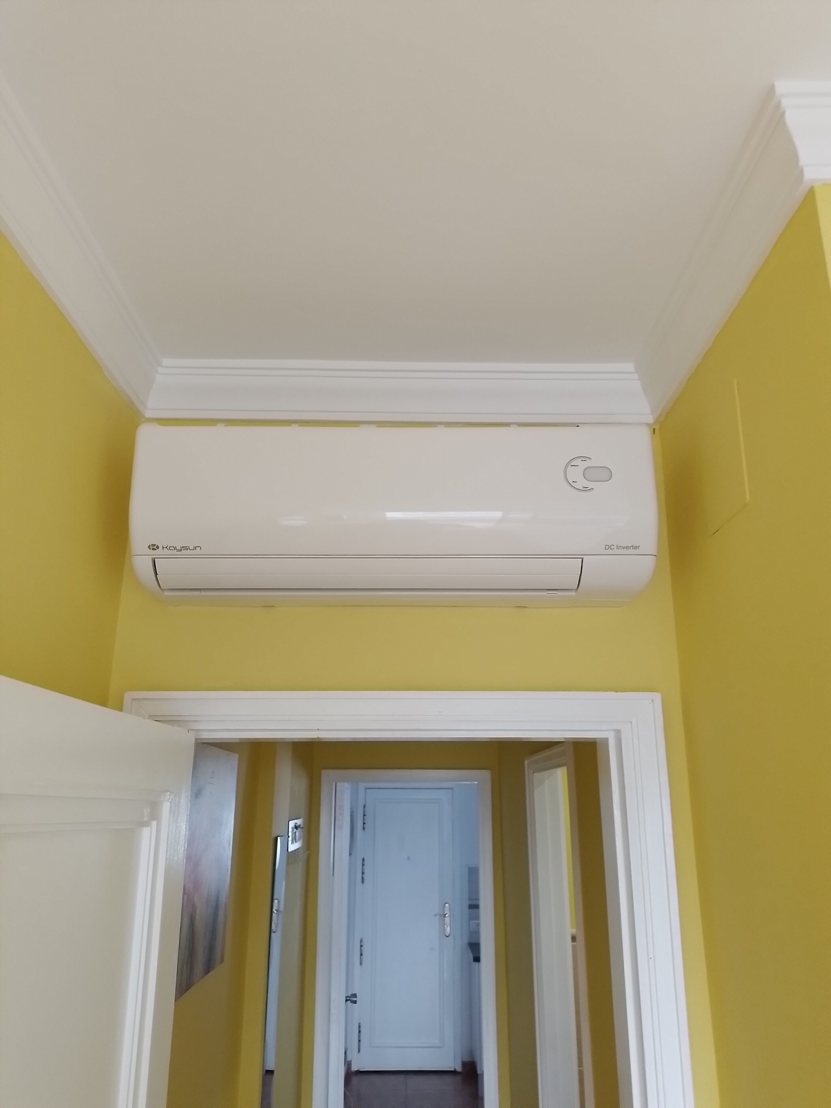 A hallway with a white door at the end, a white ceiling, and a white air conditioning unit mounted on the wall.