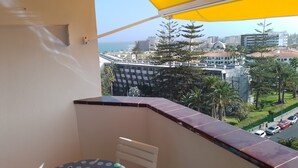 Un balcón con un toldo amarillo, vista a un paisaje urbano y una mesa con mantel de lunares.