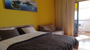 Un dormitorio con cama, sofá, un cuadro y vistas al exterior.