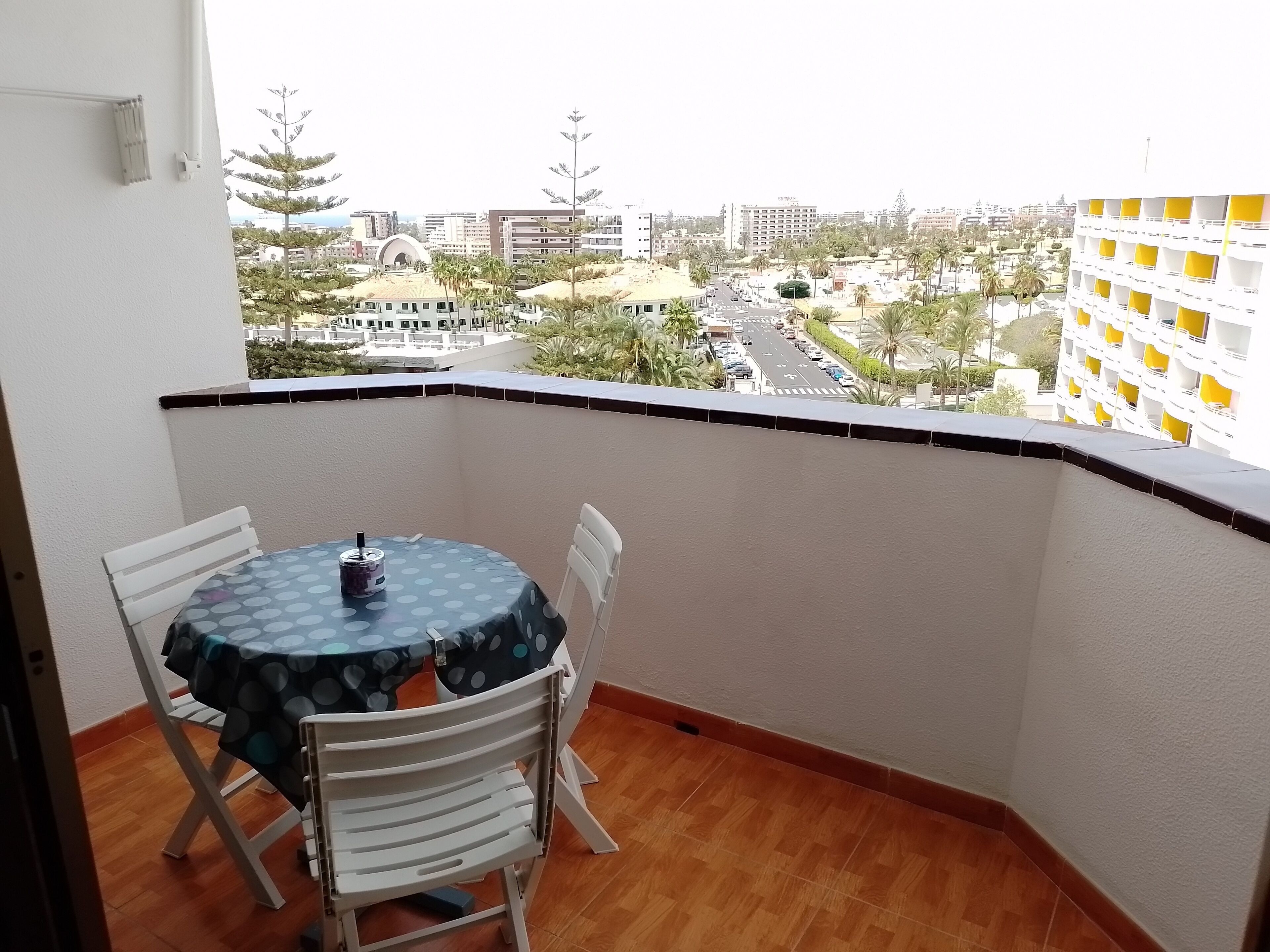 Un balcón con mesa y sillas, con vistas a un paisaje urbano con edificios y palmeras.