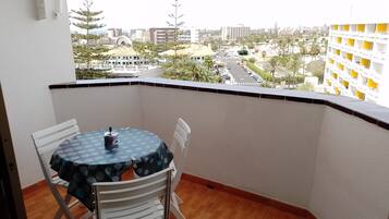 Un balcón con mesa y sillas, con vistas a un paisaje urbano con edificios y palmeras.