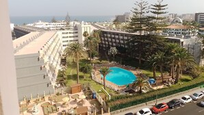 Un hotel con piscina, palmeras y vistas al mar.