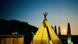 A yellow teepee with a fire inside, surrounded by a wooden structure with benches and a table. - Beautiful Teepee With Private Facilities (Zujar)