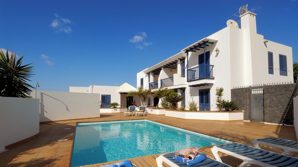 A poolside area with lounge chairs, a pool, and a two-story building with balconies. - Impeccable 2-bed Apartment No 2 in Playa Blanca (Yaiza)