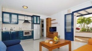 A modern kitchen with blue cabinets, a dining area with a wooden table, and a TV on a wooden stand. - Impeccable 2-bed Apartment No 2 in Playa Blanca (Yaiza)