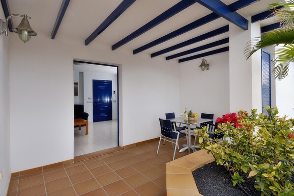 Une pièce avec un sol carrelé, une table à manger avec des chaises, une porte bleue et un petit espace jardin avec des plantes.