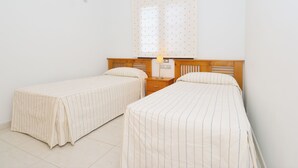 A room with two single beds, a nightstand with a lamp, and a window with a patterned curtain. - Impeccable 2-bed Apartment No 2 in Playa Blanca (Yaiza)