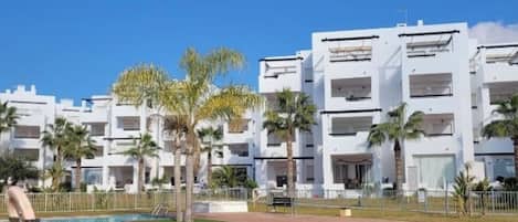 Un hôtel moderne doté d’une piscine, de palmiers et surplombant un ciel d’un bleu limpide.