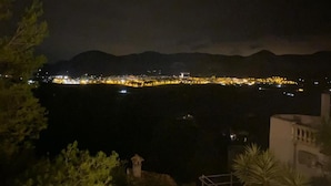 Ein nächtlicher Blick auf eine Küstenstadt mit Bergpanorama, mit beleuchteter Küstenlinie und einer markanten Kirche.