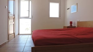 Ein Schlafzimmer mit einem Bett, einem Nachttisch, einer roten Lampe, einem Fenster und einer Tür zu einem anderen Raum.