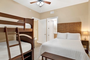 A room with bunk beds, a single bed, a ceiling fan, a bedside table with a lamp, and a door leading to another room. - Welcome to Turquoise C1408 in Orange Beach, Alabama. (Orange Beach)