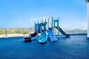 A playground with slides and climbing structures, surrounded by a white fence and a clear sky. - Welcome to Turquoise C1408 in Orange Beach, Alabama. (Orange Beach)