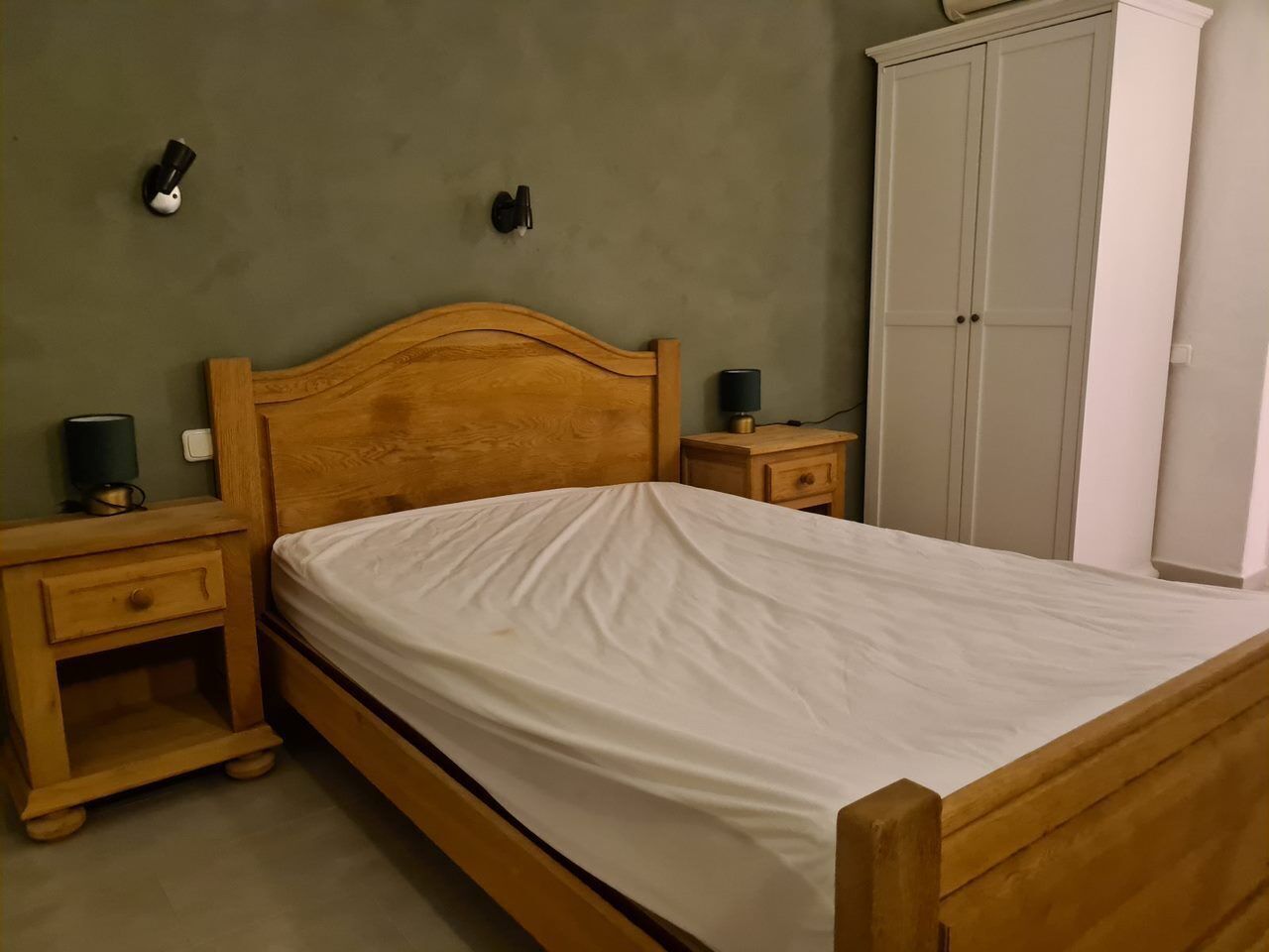 Un dormitorio con una cama de madera, una mesita de noche, un armario y dos lámparas de pared.