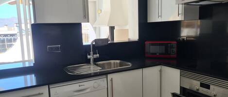 A modern kitchen with white cabinets, a black countertop, a red microwave, and a dishwasher.