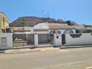 Propiedad cercada con fachada blanca, portón metálico y una montaña al fondo.