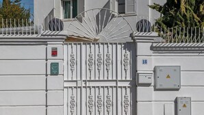 Un portón blanco con detalles ornamentales, un cartel con el número 18 y algunos cubículos de servicios en la fachada de un edificio.