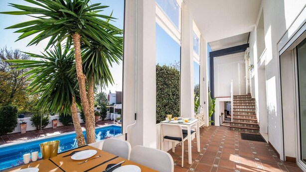 Un área de comedor con vista a la piscina, una escalera y una palmera grande.