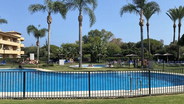 Une piscine entourée de palmiers et un bâtiment doté de balcons.