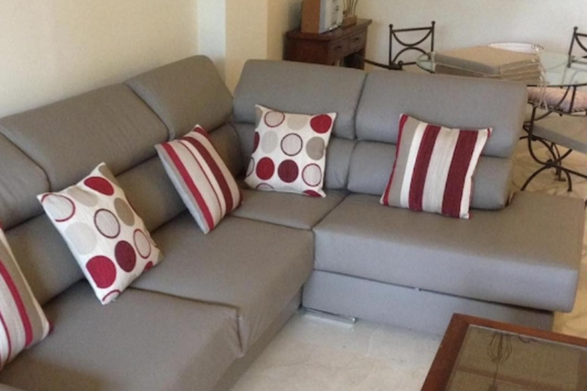 Un canapé d’angle gris agrémenté de trois coussins aux motifs rouges, blancs et gris.
