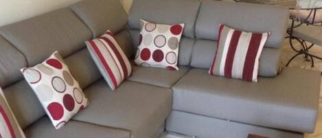 Un canapé d’angle gris agrémenté de trois coussins aux motifs rouges, blancs et gris.