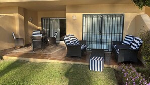 Un espace extérieur aménagé en terrasse, avec des meubles en osier, une porte vitrée et un petit jardin.