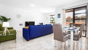 A modern living room with a blue sofa, green armchair, and dining area with a table and chairs. - House - Sleeps 6 - Pool - Pet Friendly (La Oliva)