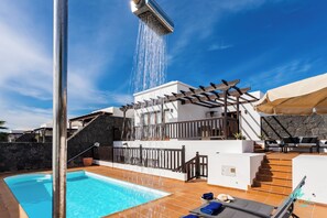 A swimming pool with a waterfall feature, outdoor seating, and a stone wall. - 4 Bed Villa - Heated Pool, Pool Table, Bbq, Patio (Yaiza)