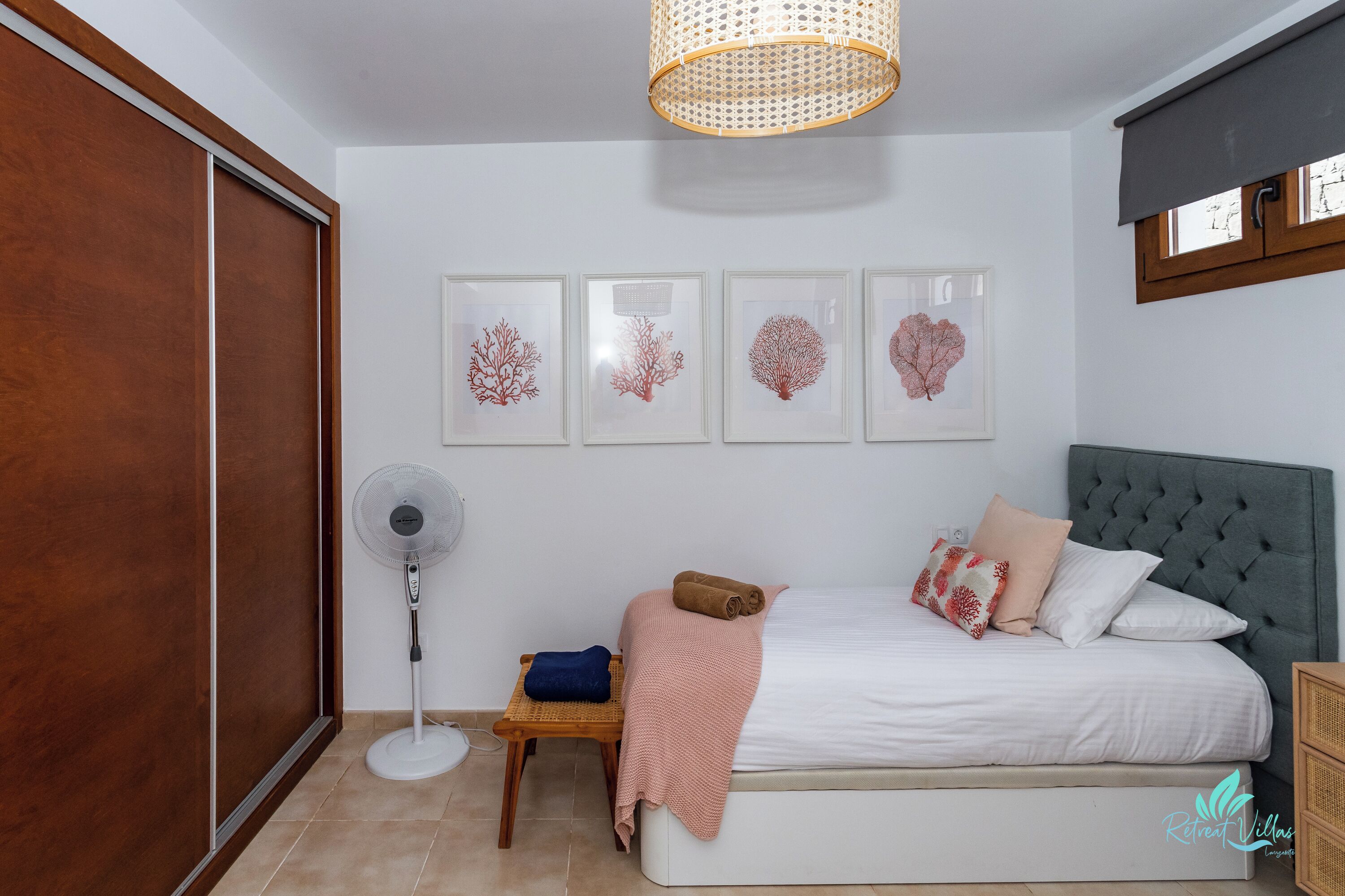 Een slaapkamer met een bed, een ventilator, een houten tafel en wanddecoratie.
