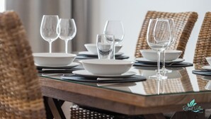 Een eettafel is gedekt met witte borden, kommen en glazen wijn, omringd door rieten stoelen.