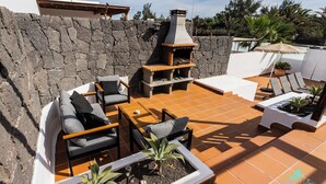 Een terras met een stenen muur, buitenmeubels, een barbecue en potplanten.