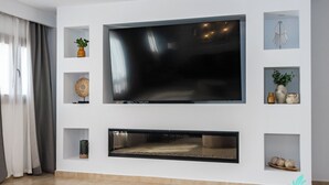 Een moderne woonkamer met een grote flatscreen televisie aan een witte muur, omringd door planken met decoratieve objecten.