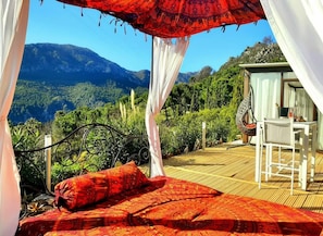 Un lit avec une couvre-lit et des oreillers à motifs rouges, un baldaquin blanc et une vue sur un paysage montagneux.