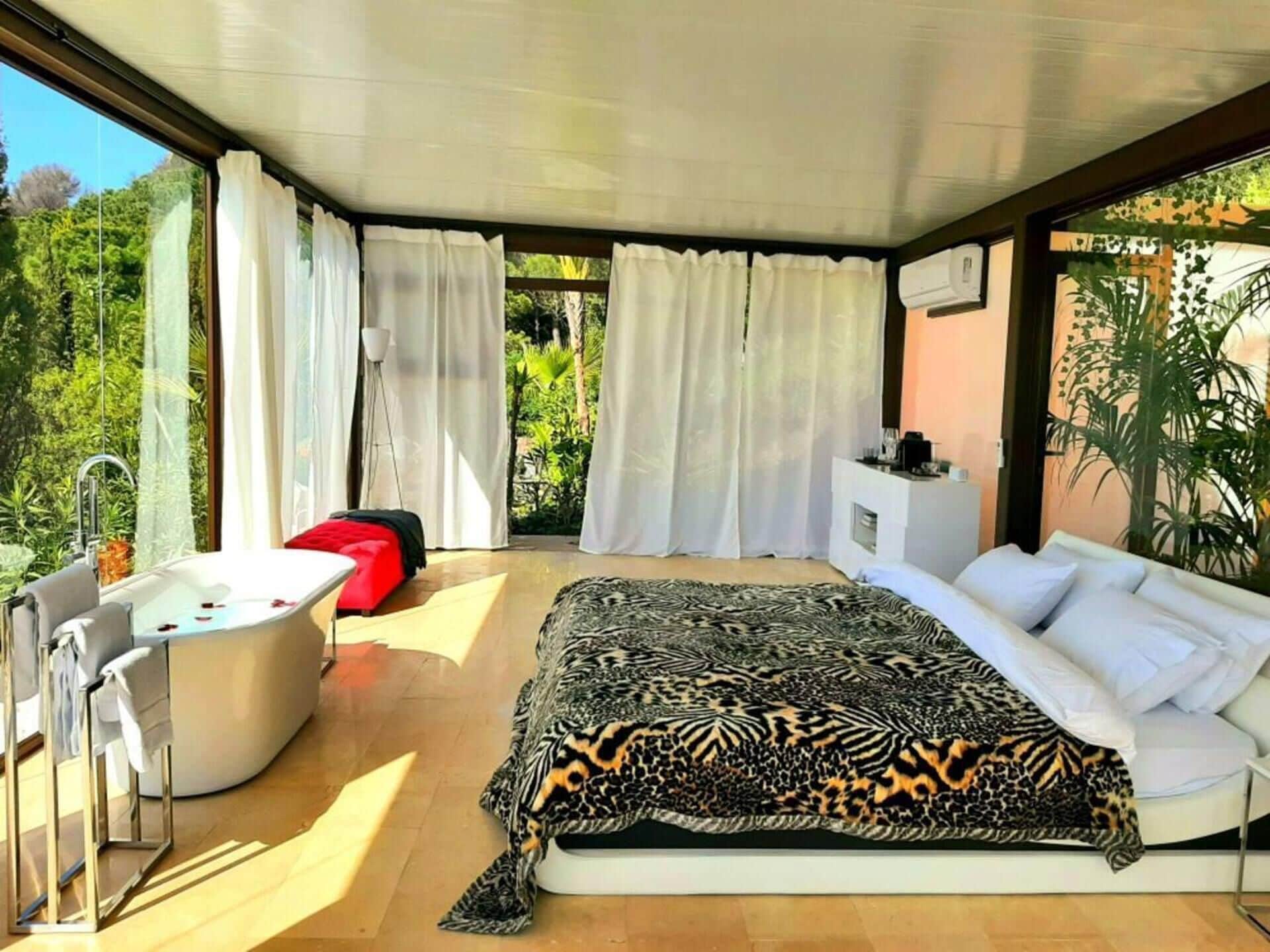 A modern bedroom with a large bed, a sitting area, and a bathtub.