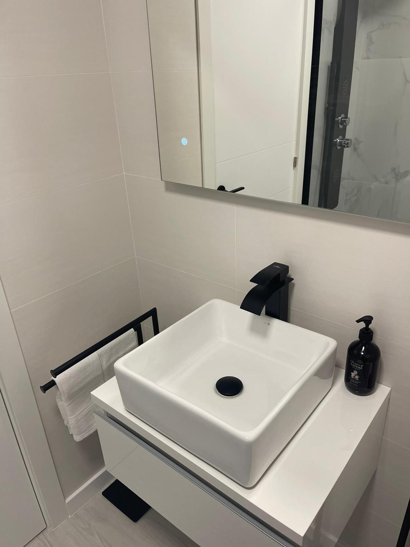 A modern bathroom with a white sink, a towel rack, and a mirror.