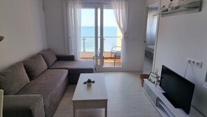 Een moderne woonkamer met een bank, salontafel, televisie en balkon met uitzicht op zee.