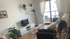 Ένα σαλόνι με έναν καναπέ, ένα τραπεζάκι σαλονιού, μια τηλεόραση και ένα φυτό.