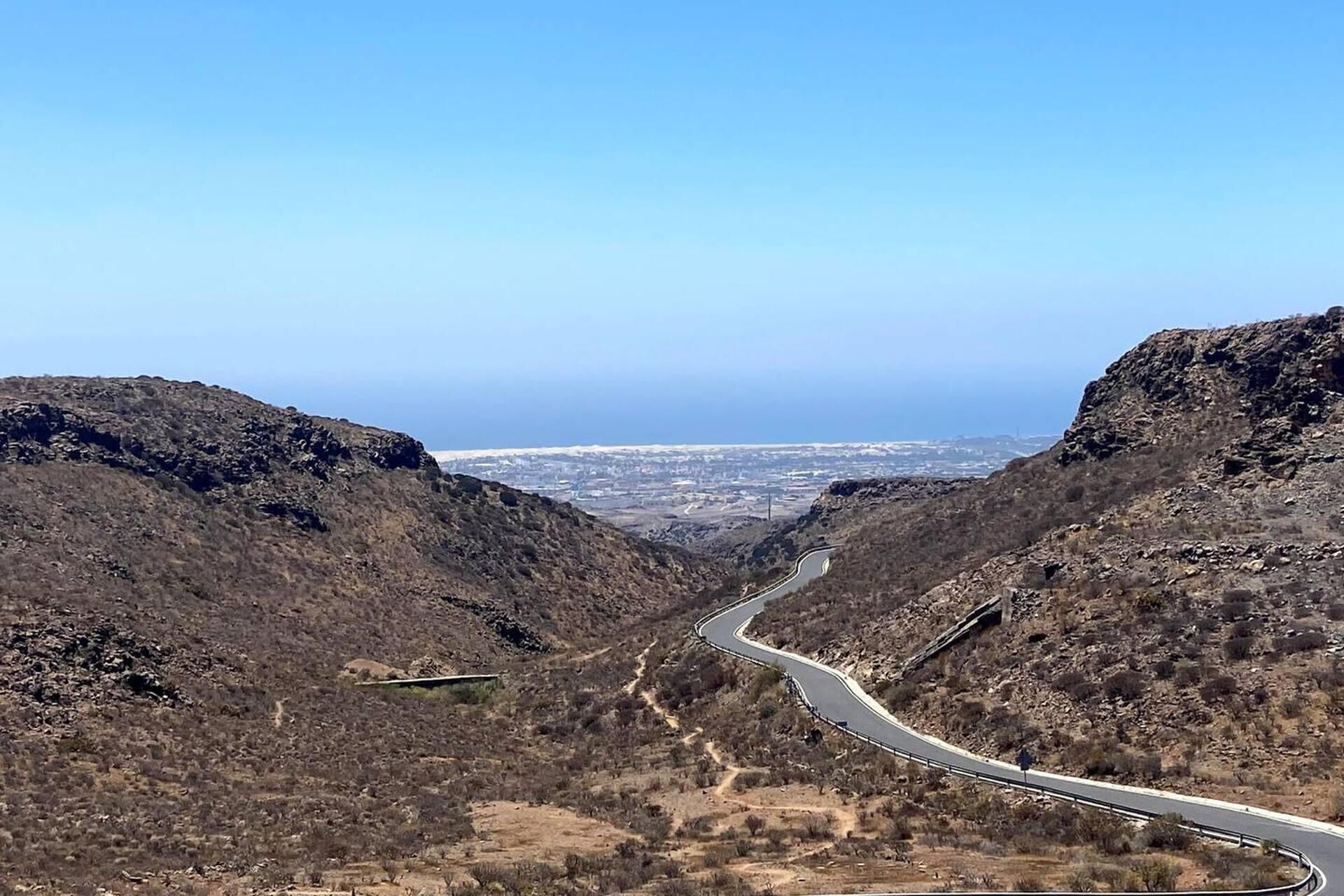 A winding road through a mountainous landscape with a clear view of a distant city.