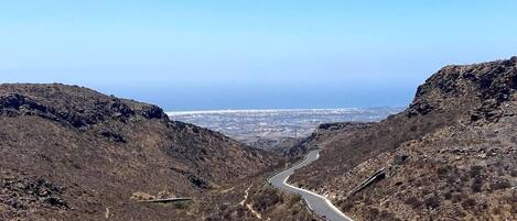 A winding road through a mountainous landscape with a clear view of a distant city.
